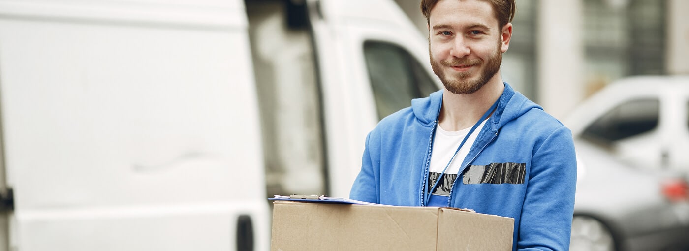A man is positioned in front of a van, gripping a box, preparing to place it inside the vehicle.