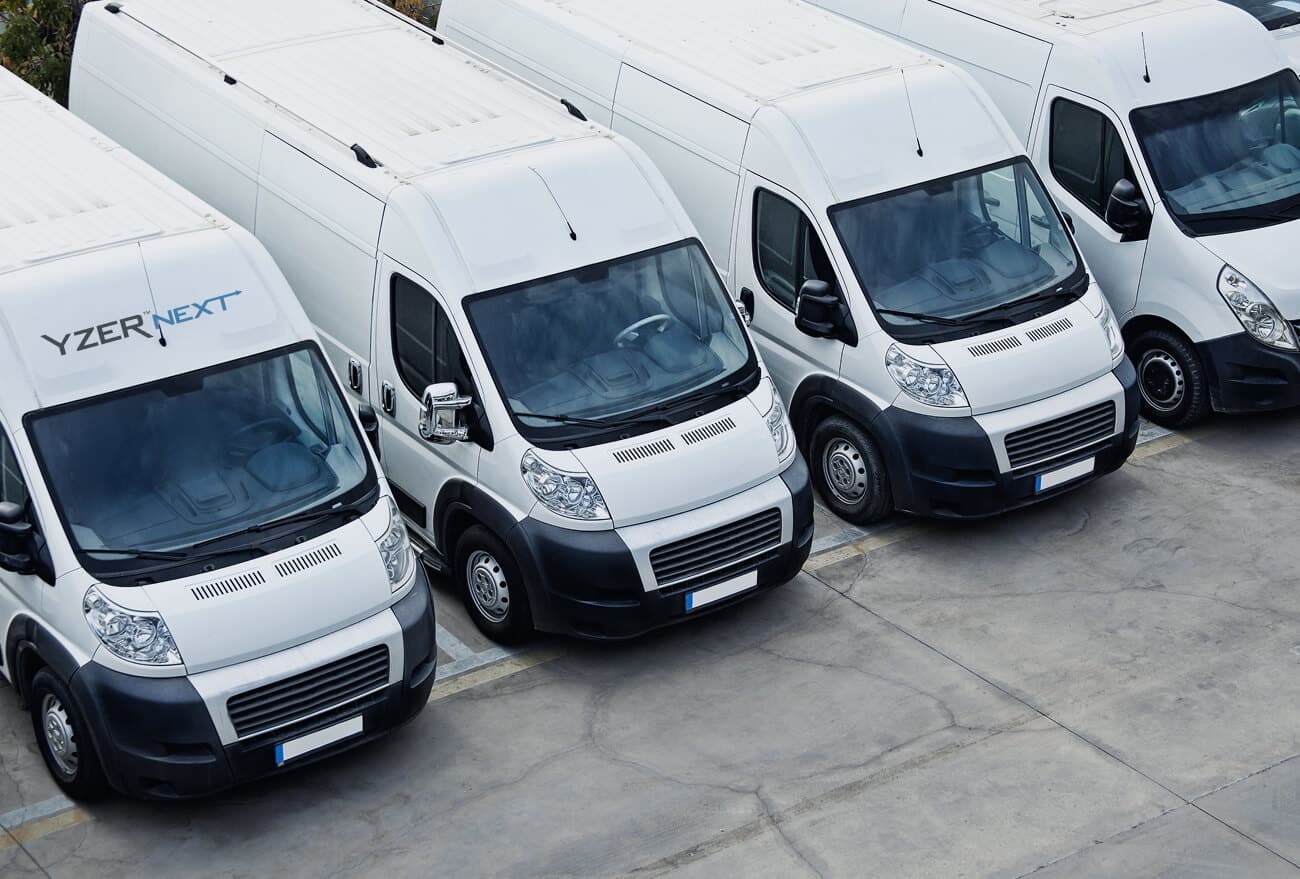 Several white vans are parked in a warehouse.